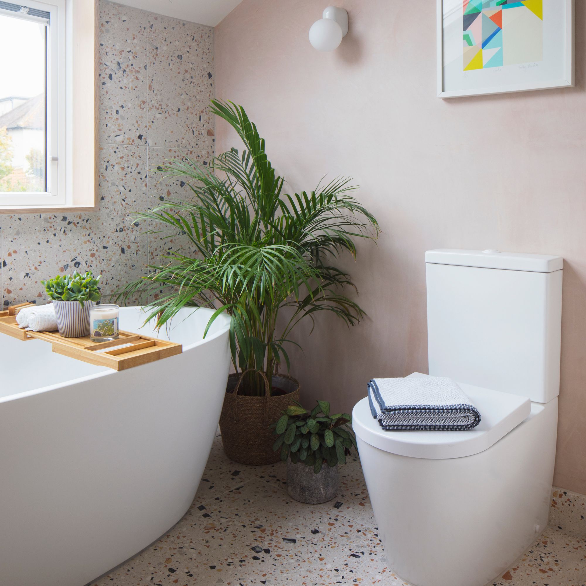 Pink painted bathroom with white freestanding bath and toilet, with terrazzo tiled floor