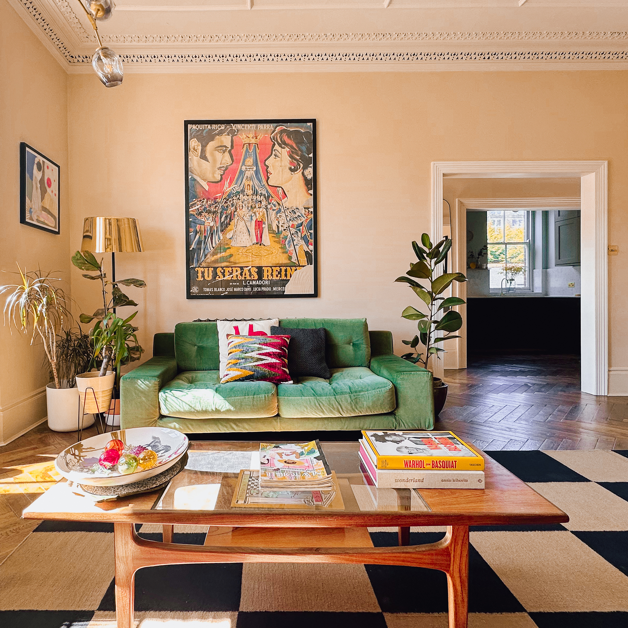 Soft pink living room with green velvet sofa and vintage coffee table, that sits of a large black and white checkerboard rug