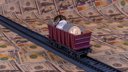 A toy train filled with coins on a track on top of hundred-dollar bills.