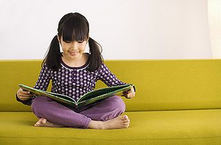 A young girl reading a book on a sofa