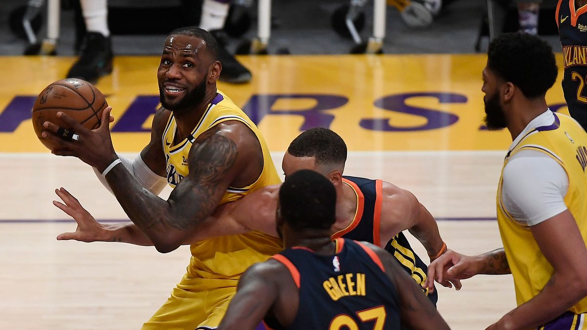 LeBron James #23 of the Los Angeles Lakers controls the ball as Draymond Green #23 and Stephen Curry #30 of the Golden State Warriors defend during the first half of an NBA Tournament Play-In game at Staples Center on May 19, 2021 in Los Angeles, California.