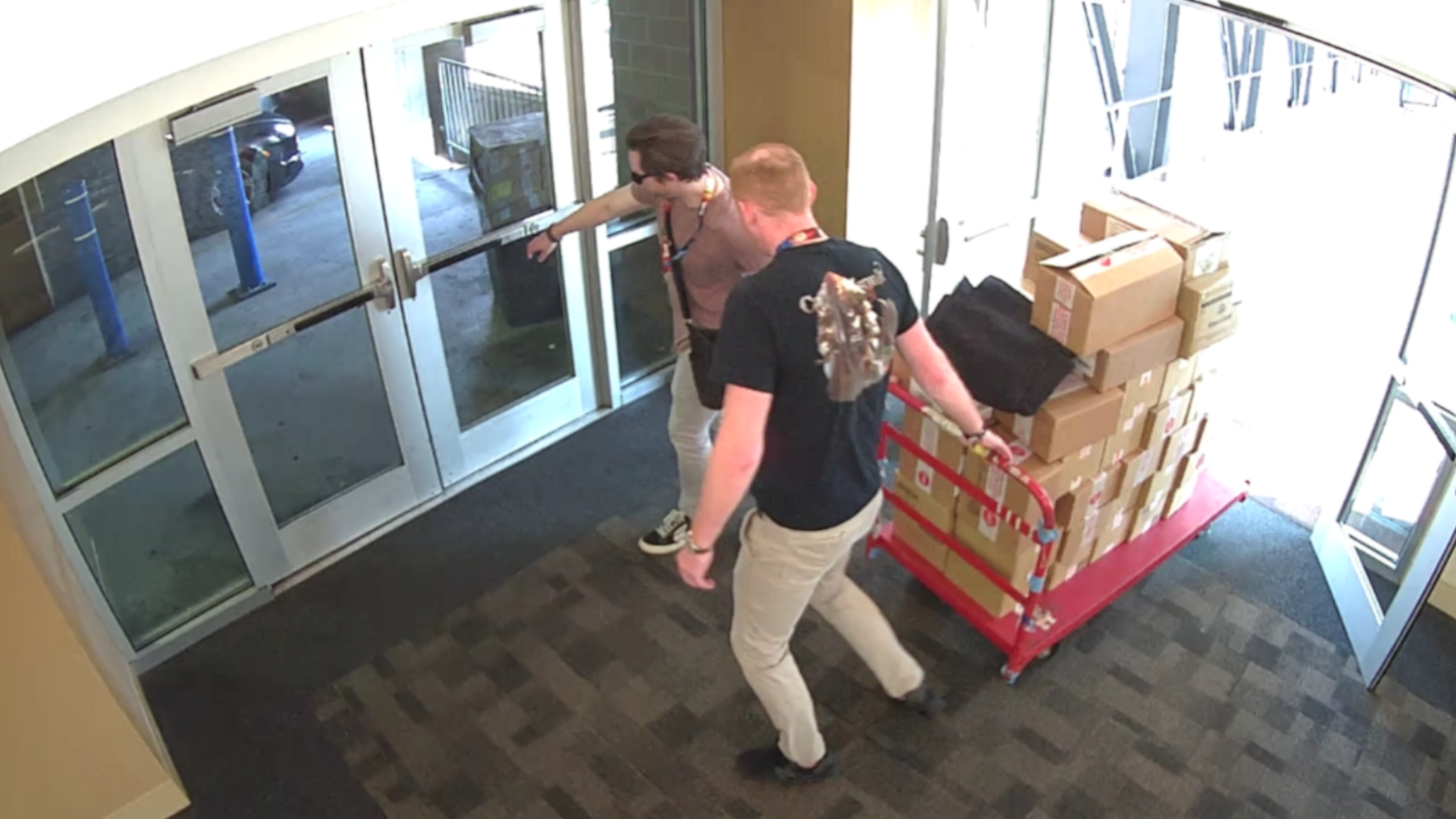 Two potential suspects in the Gen Con 2023 card heist wheel a pallet of cards out of the building. One is wearing what might be 