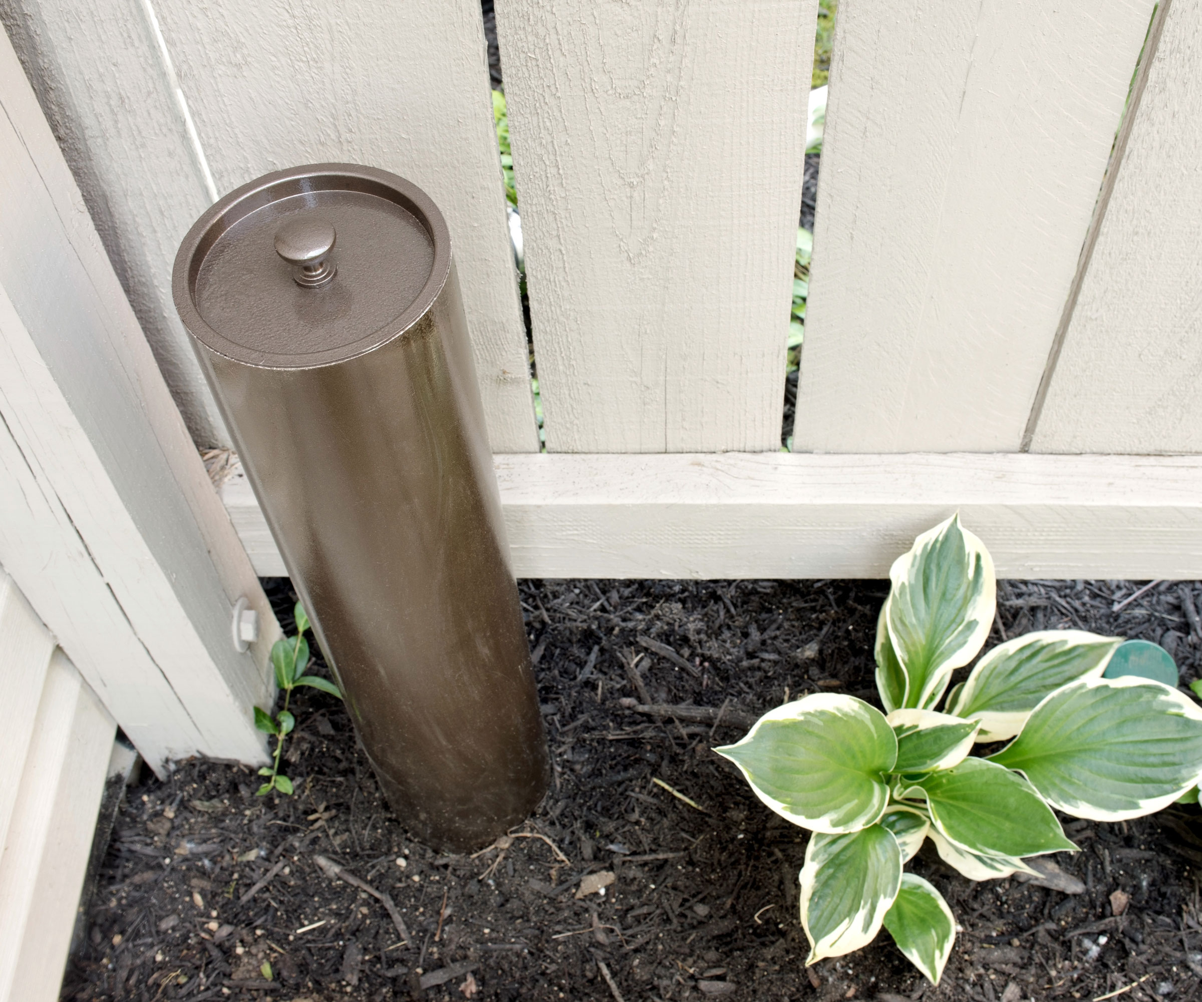 worm composting tower in corner of garden near white fence and hosta plant