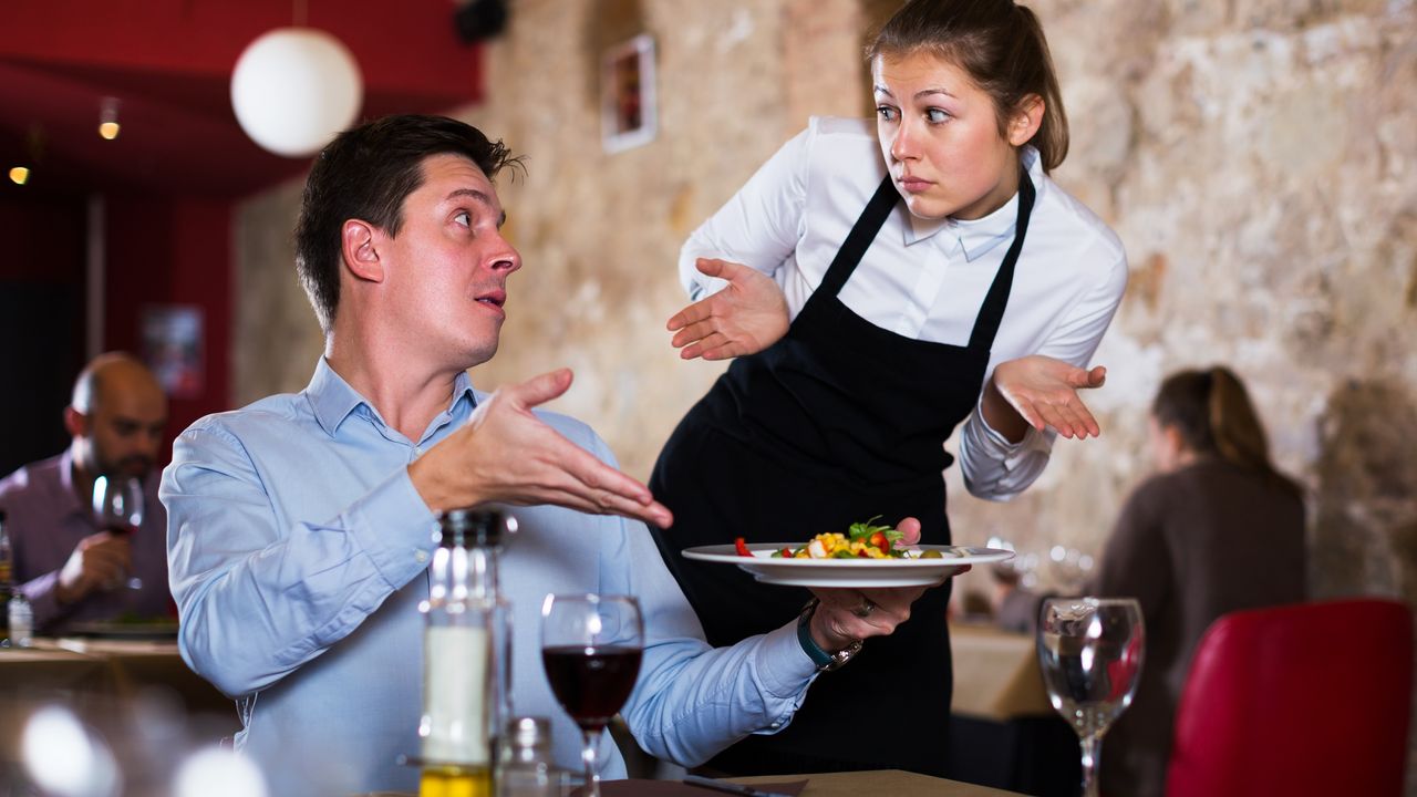 An unhappy customer gestures to his plate while a waitress shrugs.