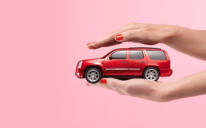 Close up of person holding a small car between their hands on a pink background