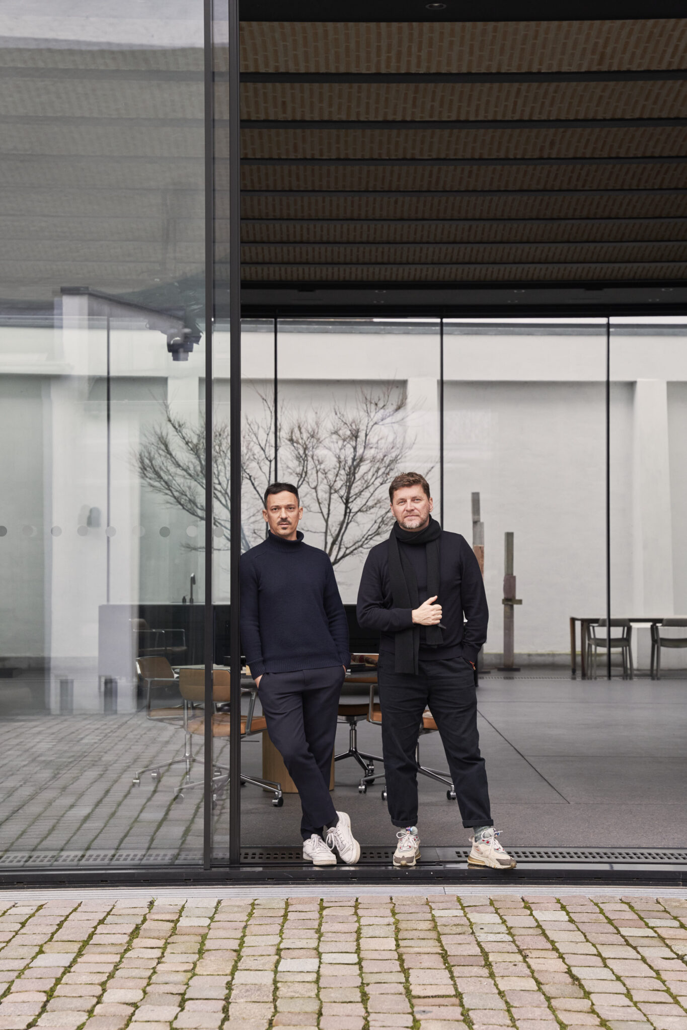 two men standing in courtyard next to a glass screen