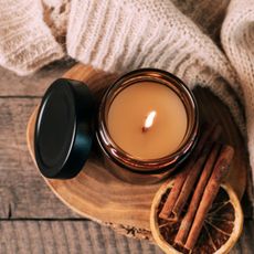 a cosy candle on a piece of wood, next to cinnamon and a cosy jumper