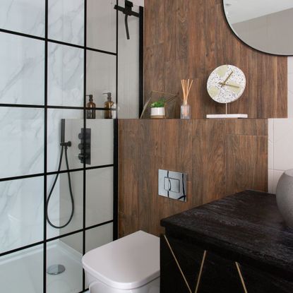 bathroom with walk-in-shower with a black screen, wooden wall with shelving and white toilet 