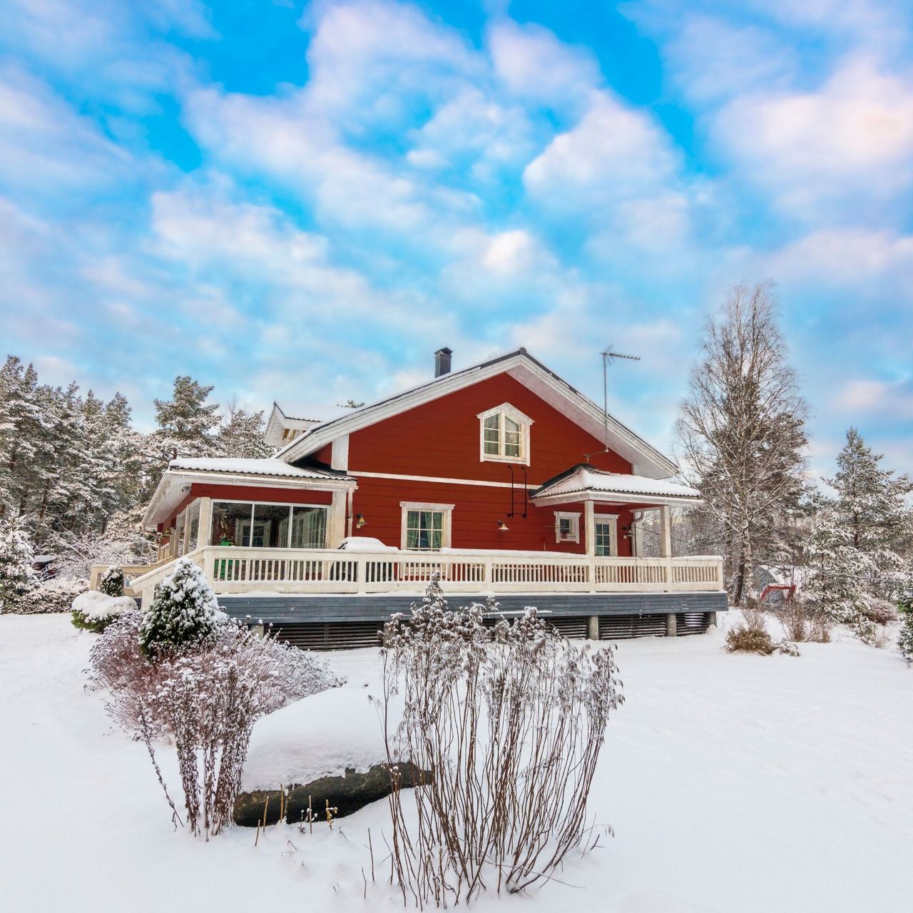Beautiful idyllic red log cabin and blue sky at winter. Garden covered in snow.