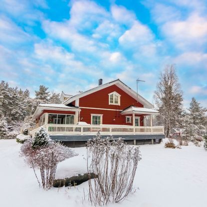 Beautiful idyllic red log cabin and blue sky at winter. Garden covered in snow.