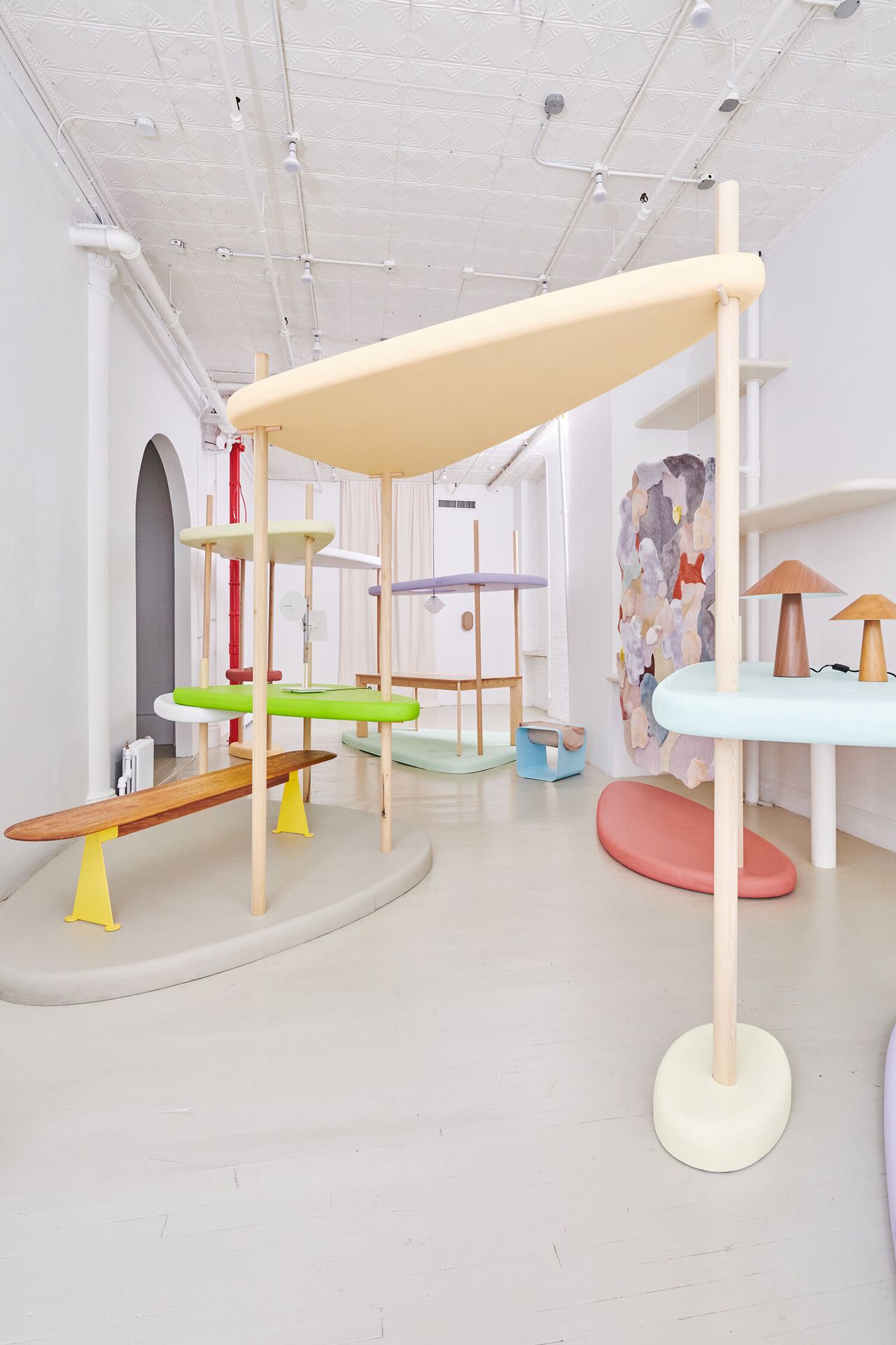 An exhibition space features sculptural furniture pieces in different pastel-shaded hues.