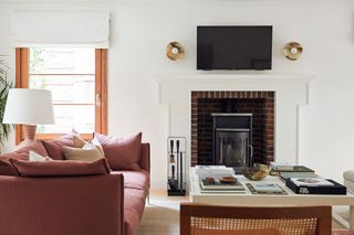 living room with white walls red sofa low white coffee table brick edged fireplace white roman blind
