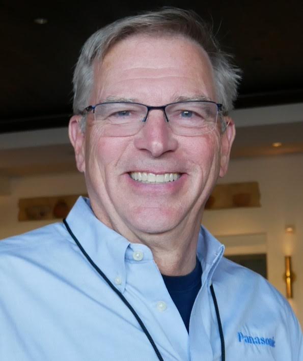 Headshot of Ken Nelson in light blue shirt in front of out-of-focus interior home background