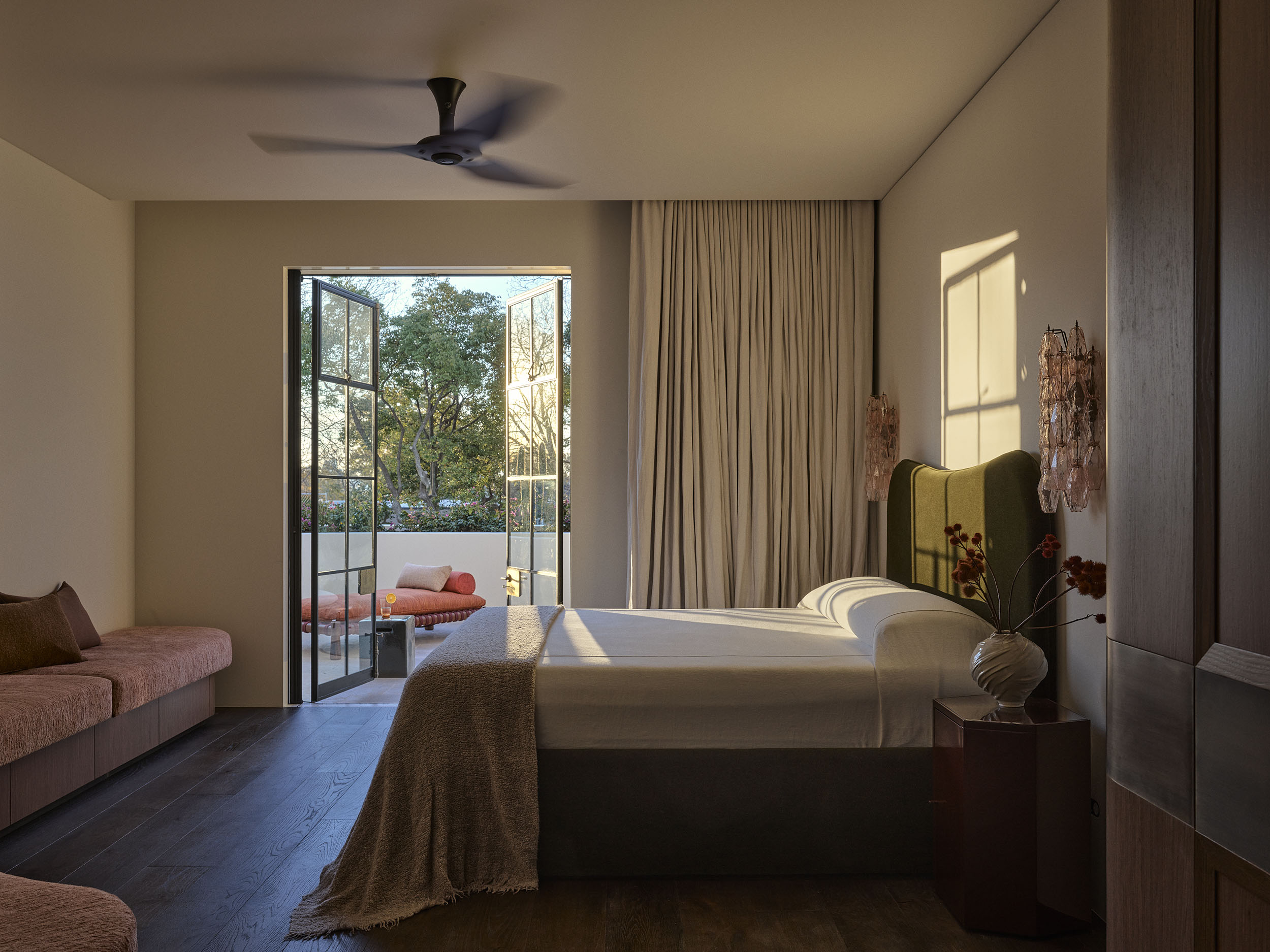 Primary bedroom in Smac Studio's renovated Art Deco home in Woollahra, Sydney, featuring warm timber joinery, sculptural lighting and steel-framed doors opening onto a private terrace.