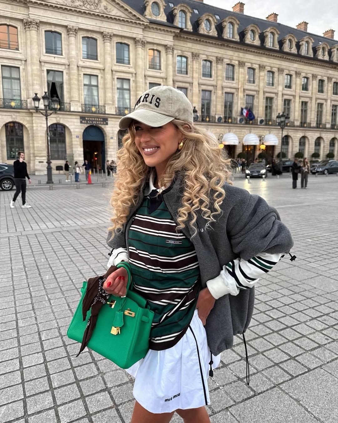 Woman in gray sporty jacket, striped t-shirt, and skirt.