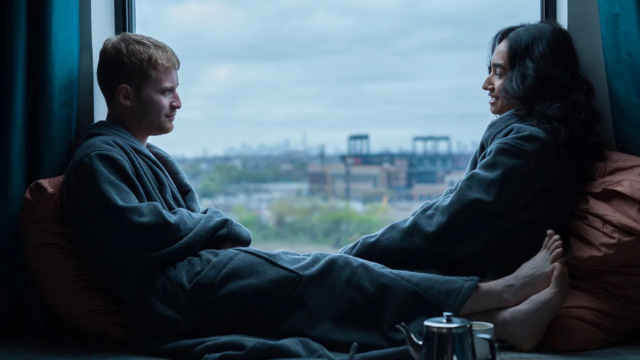 Two people (Fred Hechinger as Skinner and Sebiye Behtiyar as Aishe) sit with their legs up in a bay window, in the romance movie 'Preparation for the Next Life.'