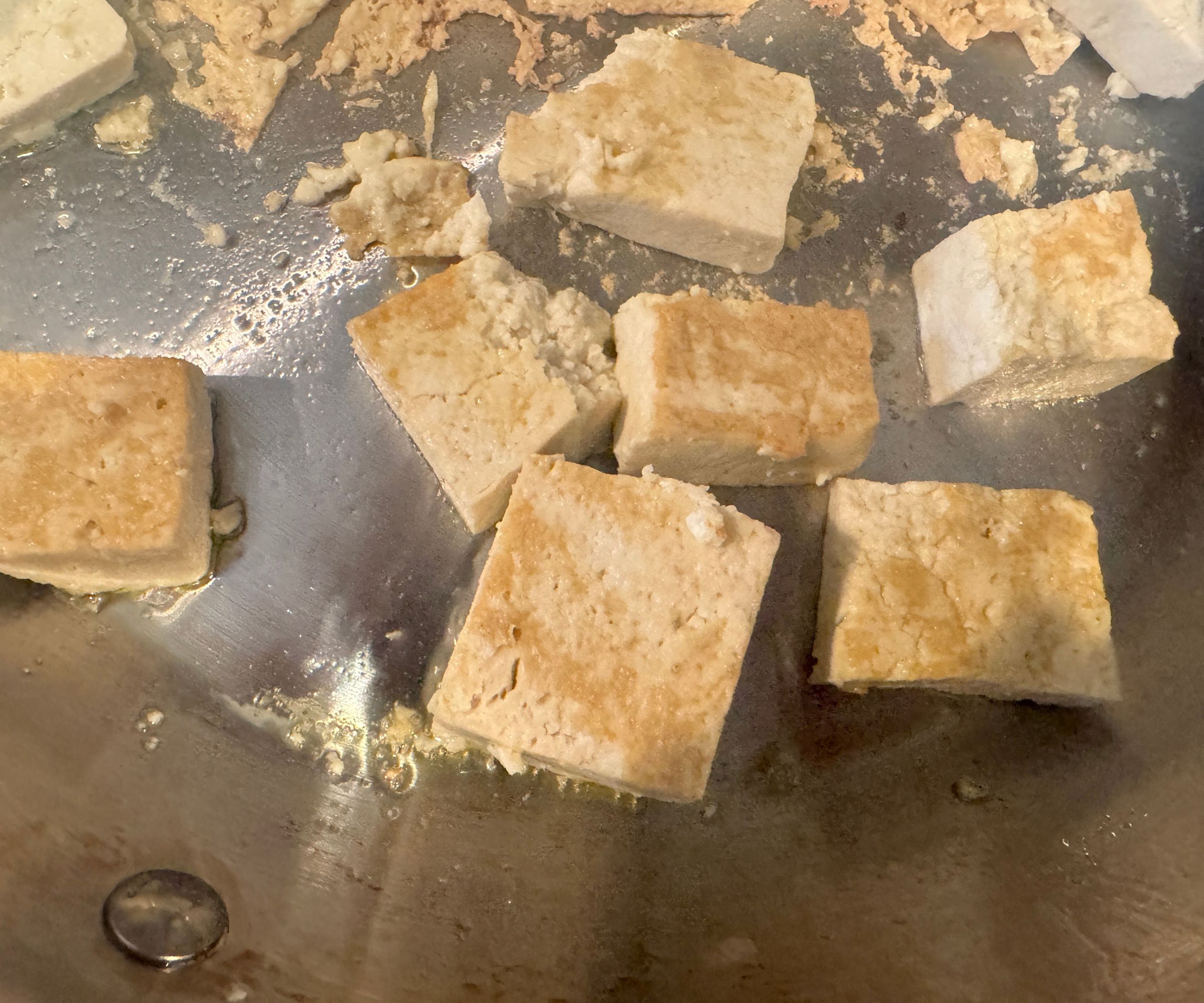 Golden brown chunks of tofu in a stainless steel frying pan. 