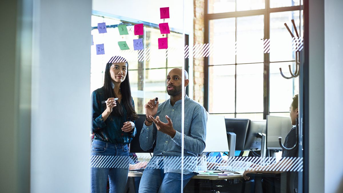 Two colleagues sitting in an office looking at sticky notes on the wall