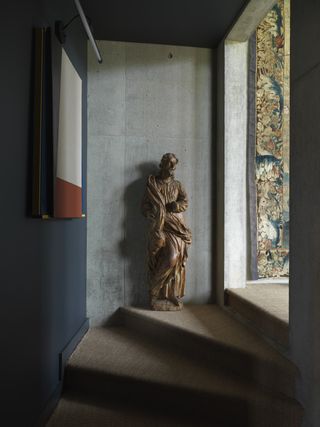 A staircase with a brown carpet, a statue, a wall painting and a tapestry.