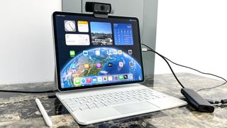 external USB webcam attached to the top of an iPad Air with Magic Keyboard showing home screen