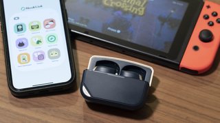 a pair of true wireless earbuds next to a smartphone and nintendo switch