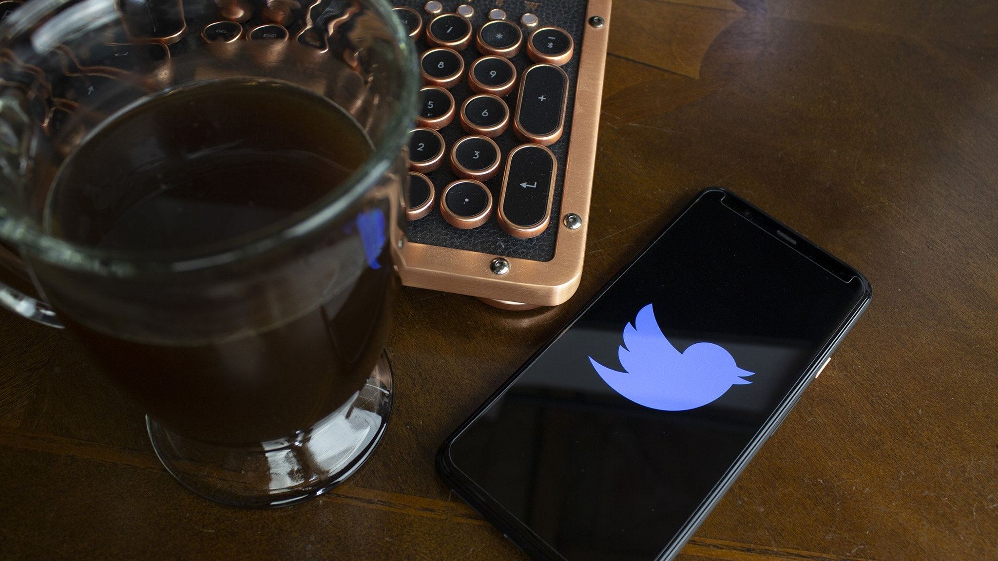 Um telefone com o logotipo do Twitter na tela, ao lado de uma xícara de café e um teclado