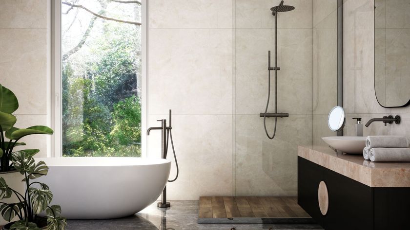 A freestanding bath with a large window showing a garden and a sink and shower to the right 