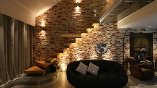 A lighting scheme in an open-plan living room and stairway with exposed brick walls