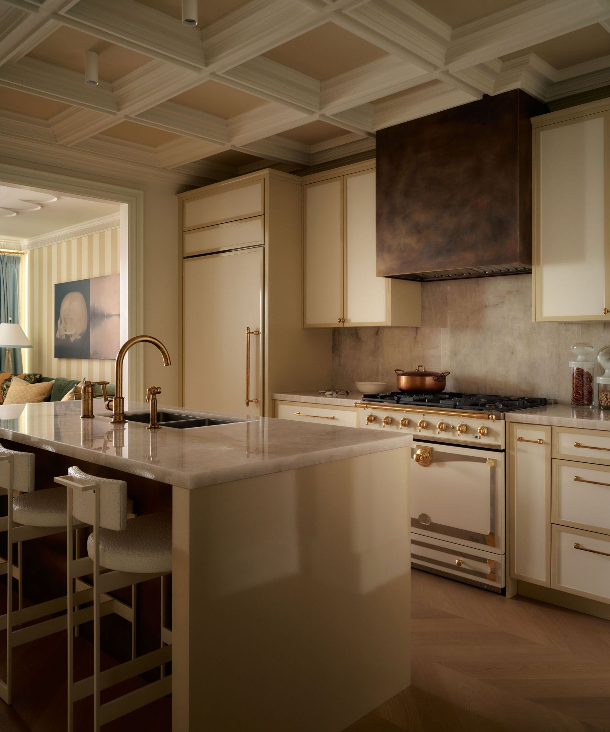 a white and gold kitchen with a brass kitchen hood, vintage style range cookr and a modern kitchen island with marble counters
