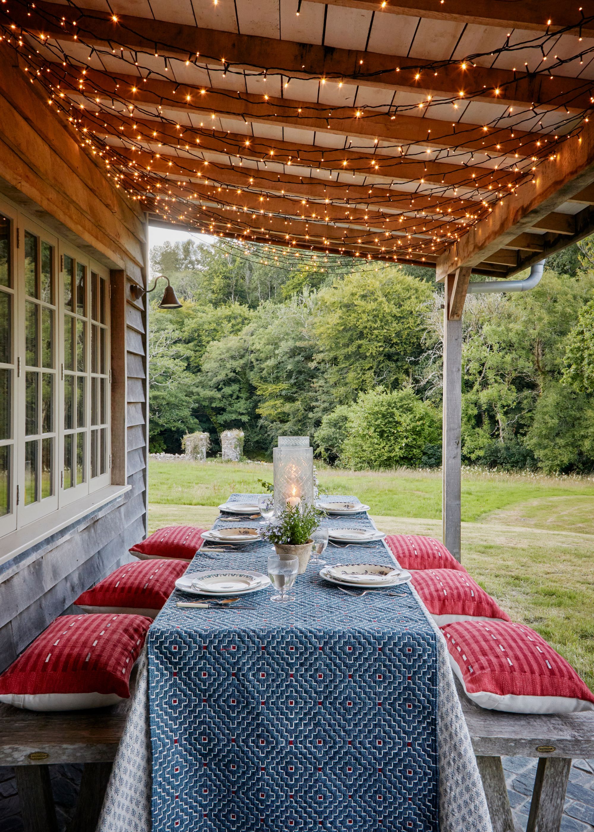 A dining table and benches on an outdoor terrace with lights on the wooden roof.