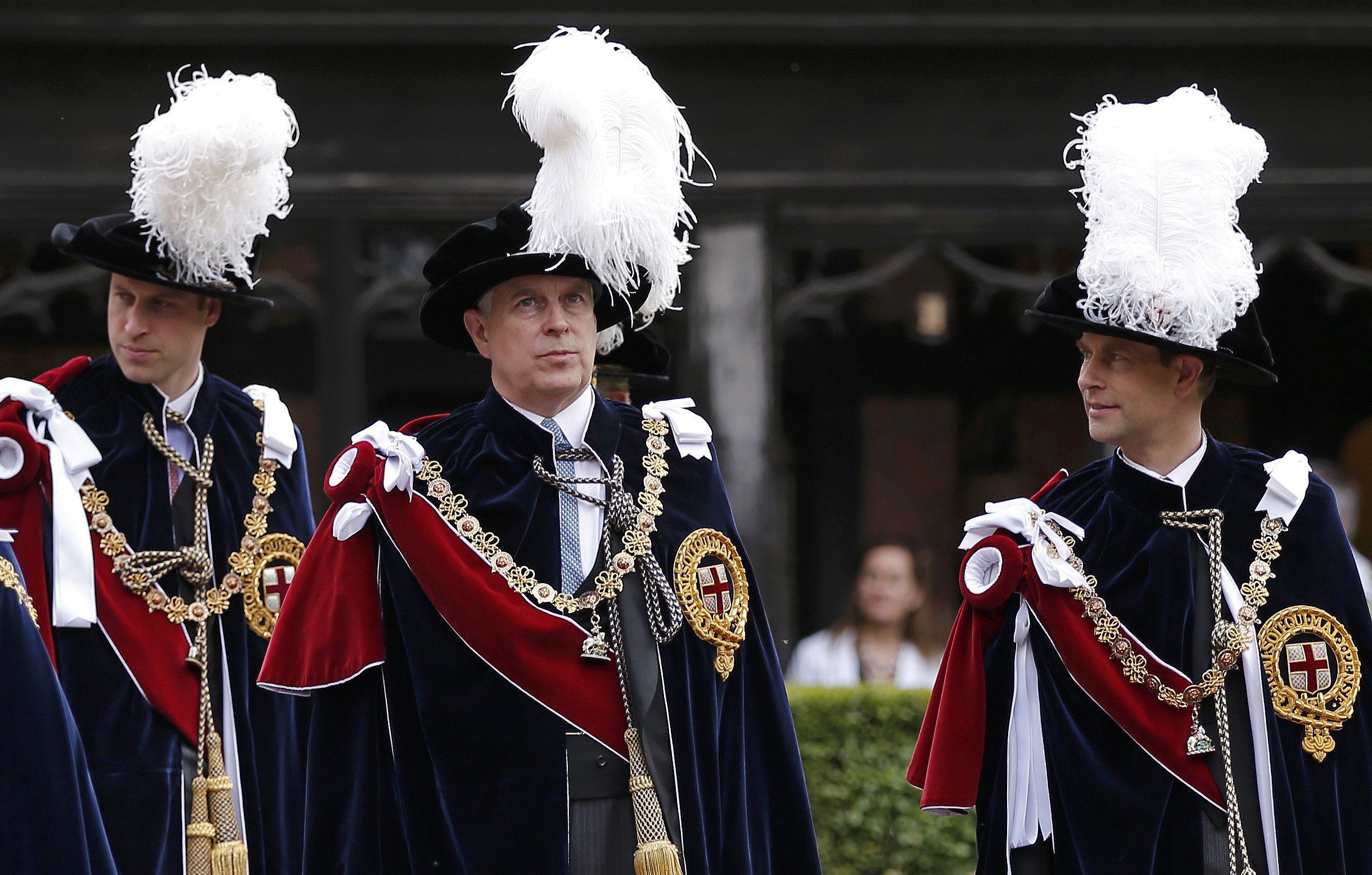 Prince Andrew attending Garter Day wearing long ceremonial robes and a black hat with a large white feather protruding from the top and a red sash and a gold chain