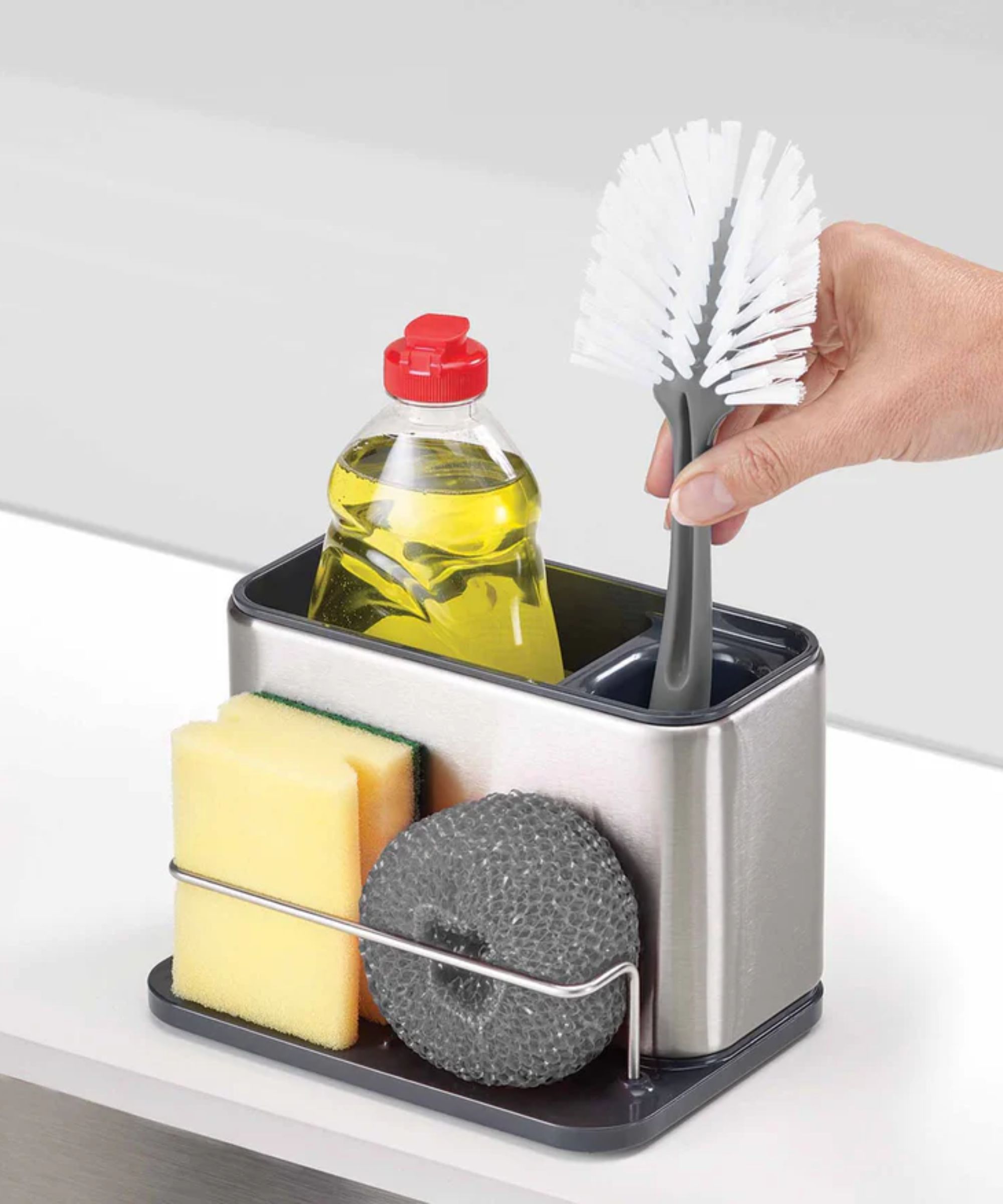 A silver sink organizing caddy with yellow dish soap, a scrubbing brush, and scouring sponges.