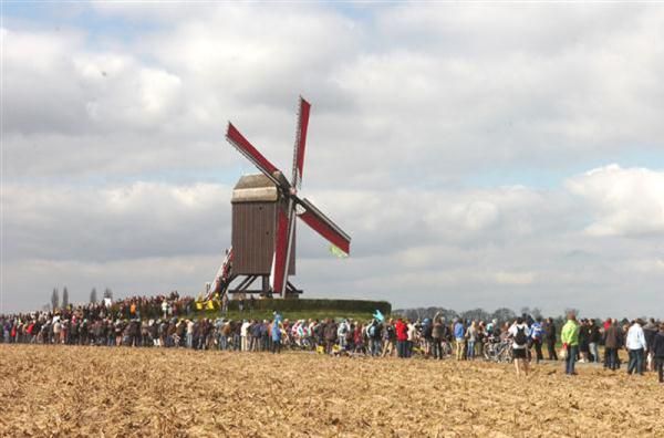 The fans watch the riders in the shadow of a windmill at the Tour of Flanders