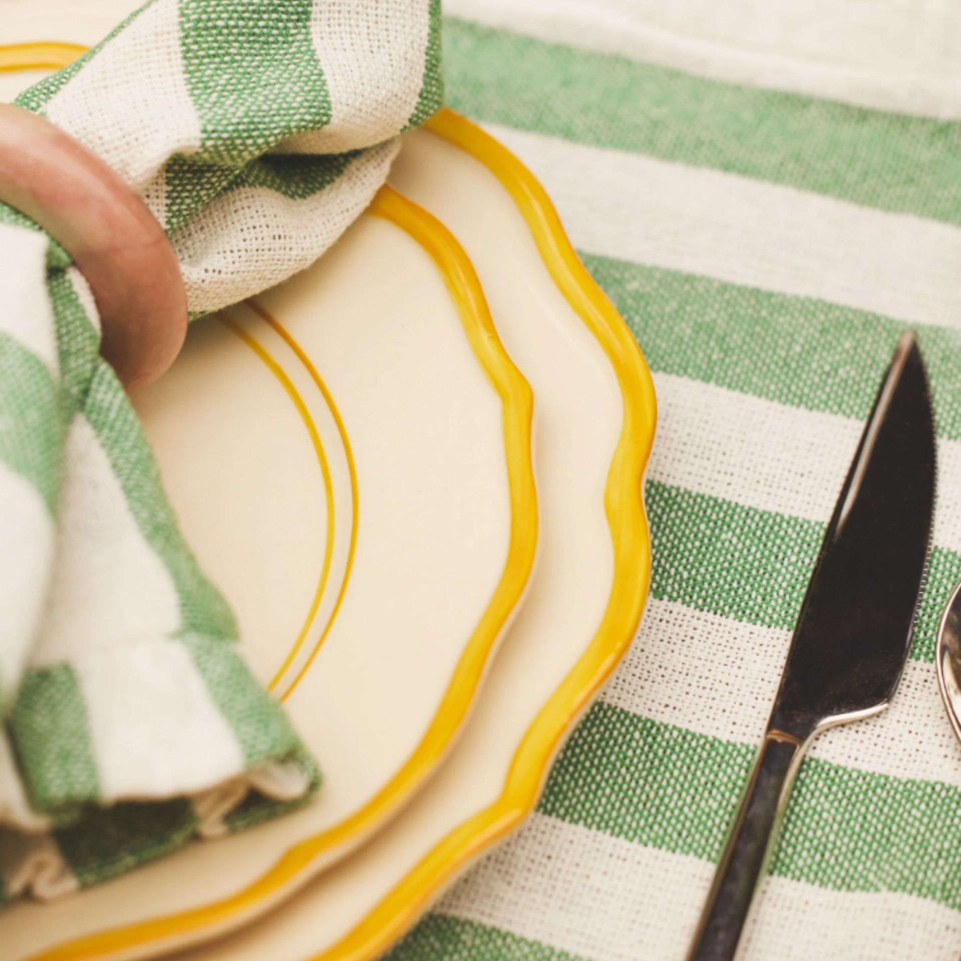 Close up of plates layered on top of each other with green and white stripe linen napkin on top and a green and white strip placemat underneath