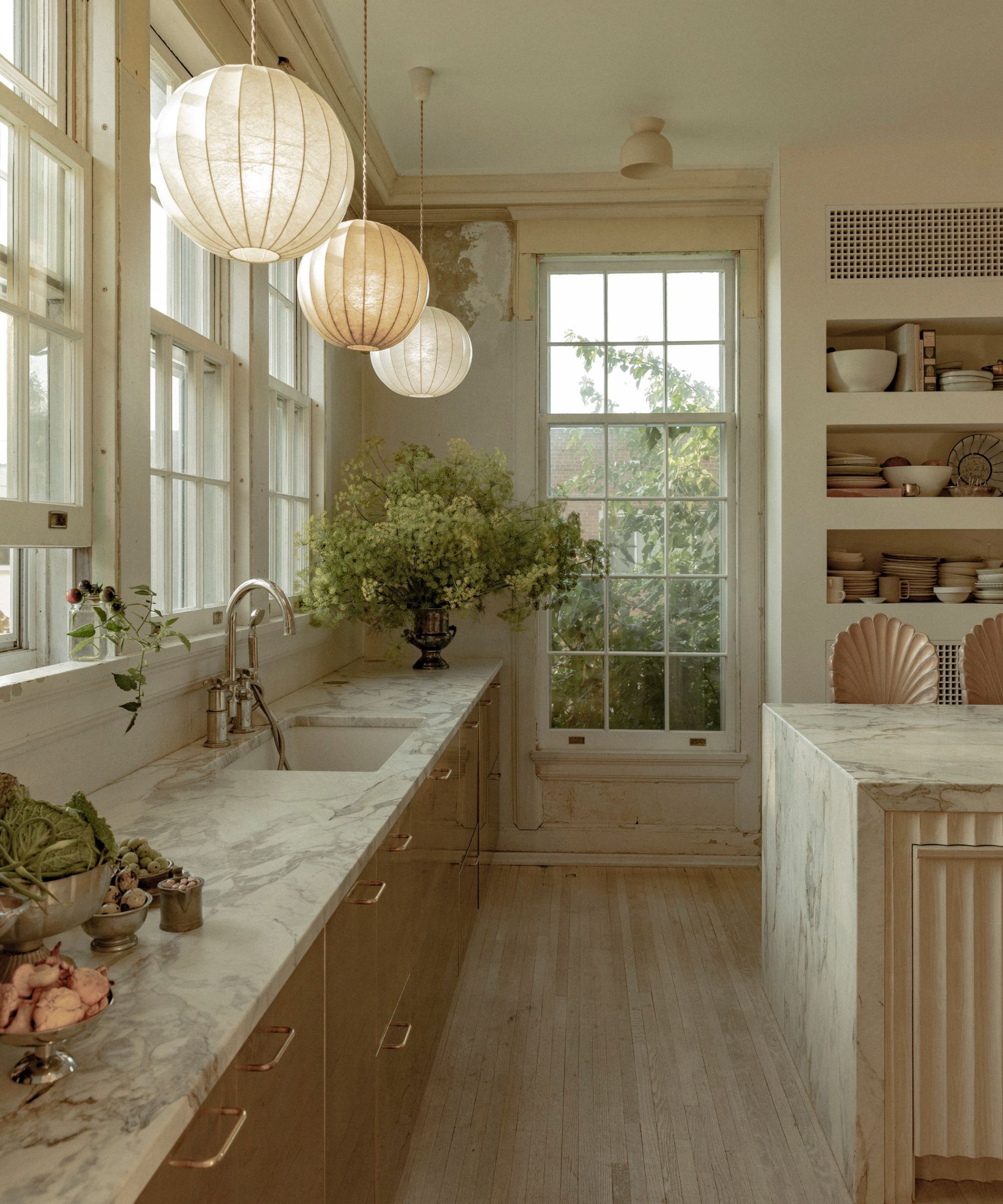 a historic kitchen in Maison Bodega, with brass cabinetry, marble counters, open shelving and silk lanterns