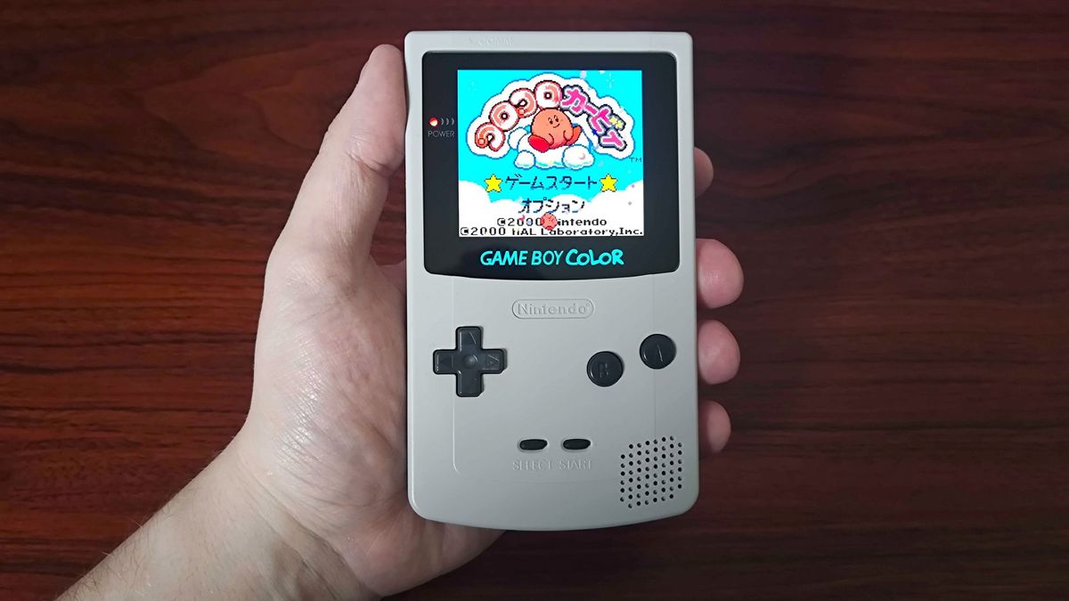 Hand holding modded Game Boy Color with white shell and AMOLED screen with Japanese version of Kirby&#039;s Tilt &#039;n&#039; Tumble on screen