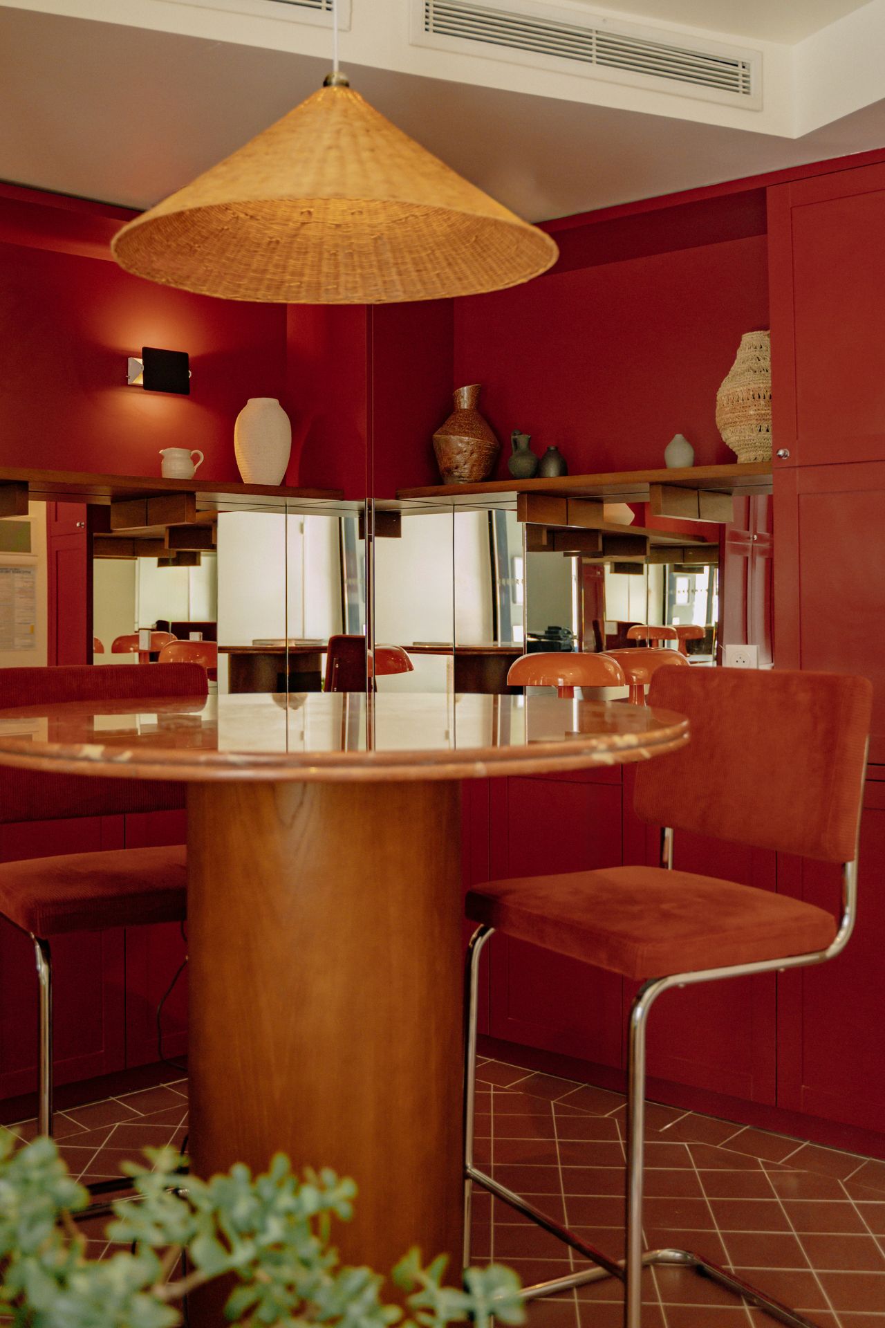 The 1970s-inspired reception of a hotel features chrome, suede, rattan, and ceramic accents, all with a terracotta color scheme.
