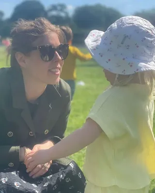 Princess Beatrice kneeling in a field talking to Sienna Mapelli Mozzi, who is wearing a yellow shirt and sun hat