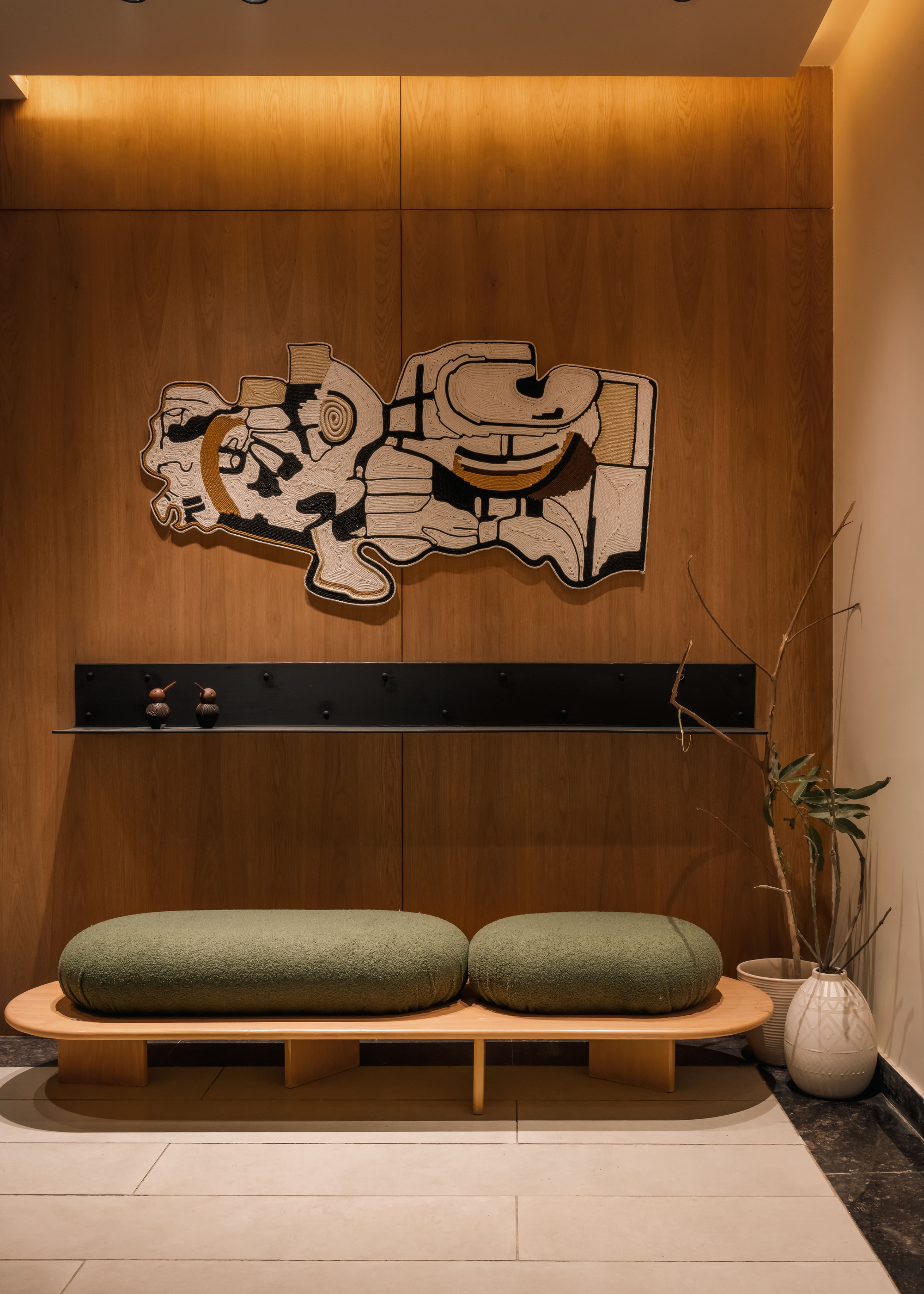 A room with a wood wall, a low bench, a potted plant, and a wall hanging