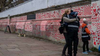 A woman hugs her son as they draw hearts on the Covid-19 Memorial Wall which is nearing completion opposite Parliament