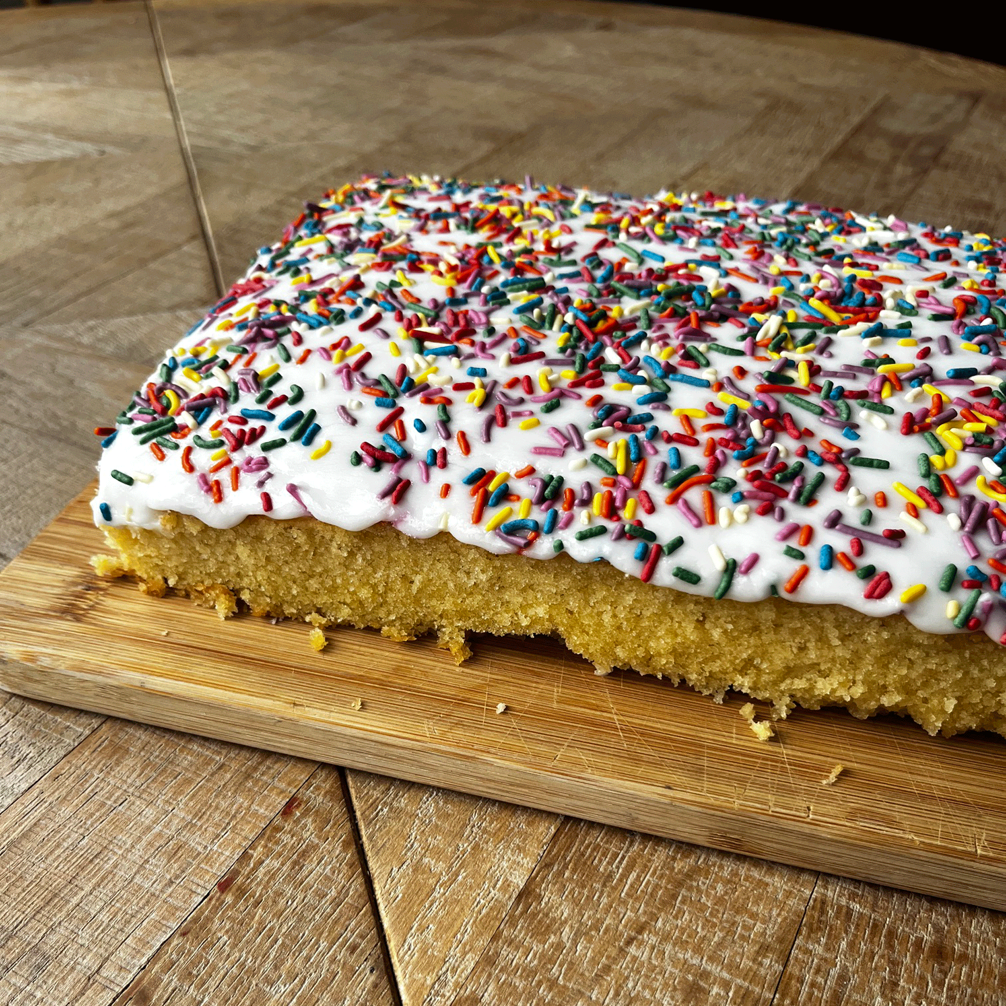 close up of a sponge cake covered in white icing and rainbow sprinkles