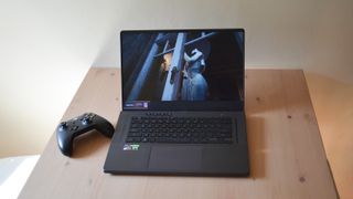En gaming-laptop av typen Asus Zephyrus G15 står åpen på en bordplate sammen med en spillkontroller.