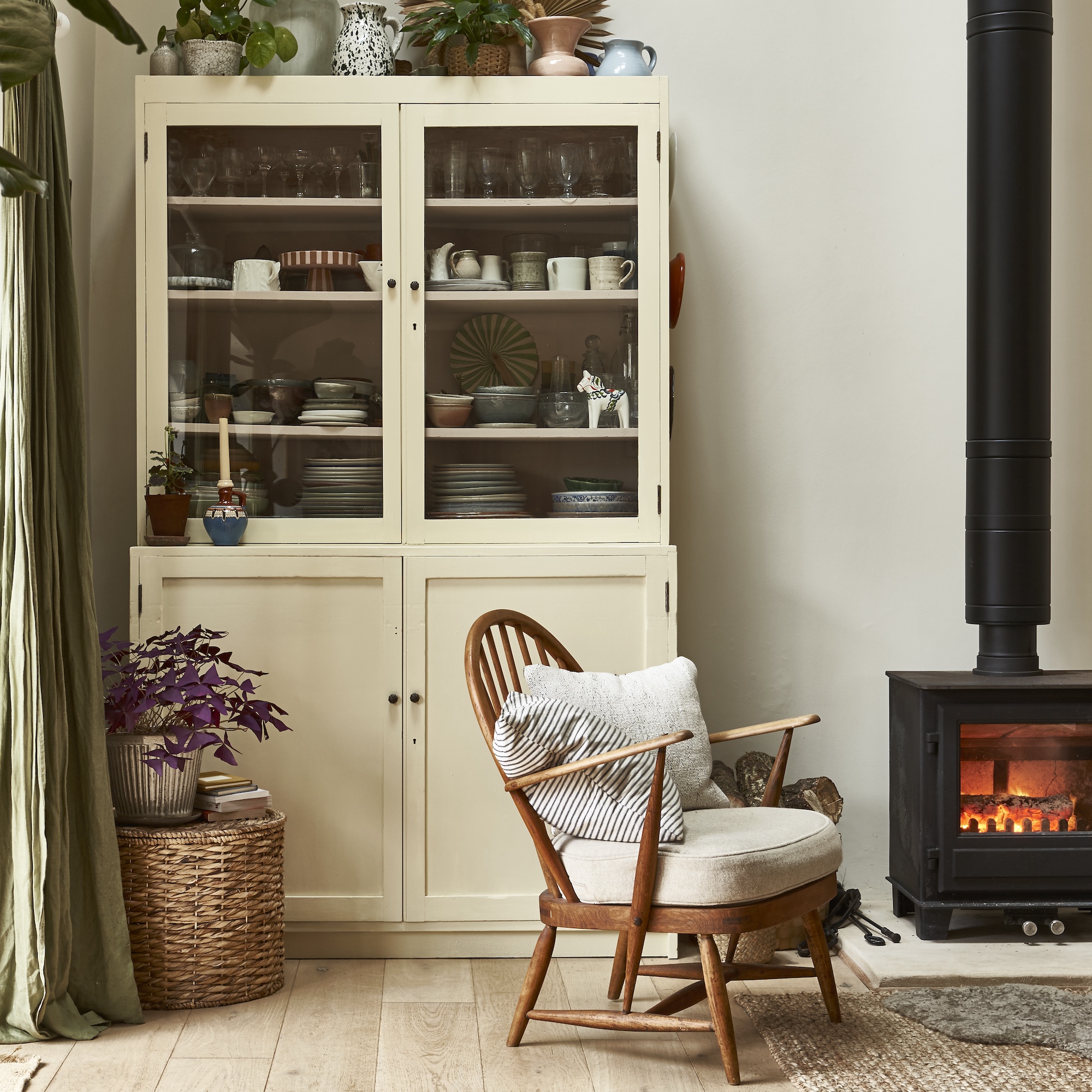 corner of living room with wood framed chair with padded seat and large glazed cabinet with plates and tableware