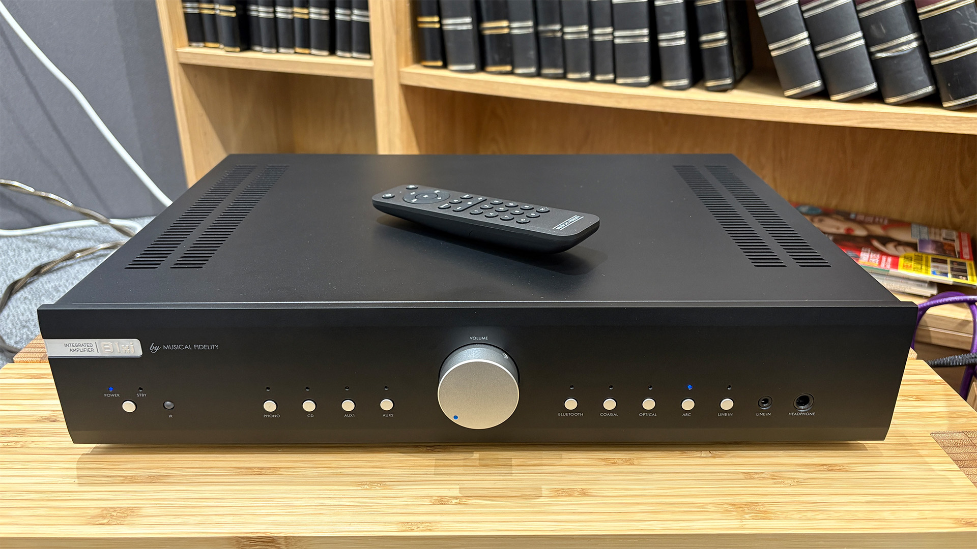 Musical Fidelity B1xi integrated amplifier on wooden hi-fi rack in front of bookcase with remote control on top