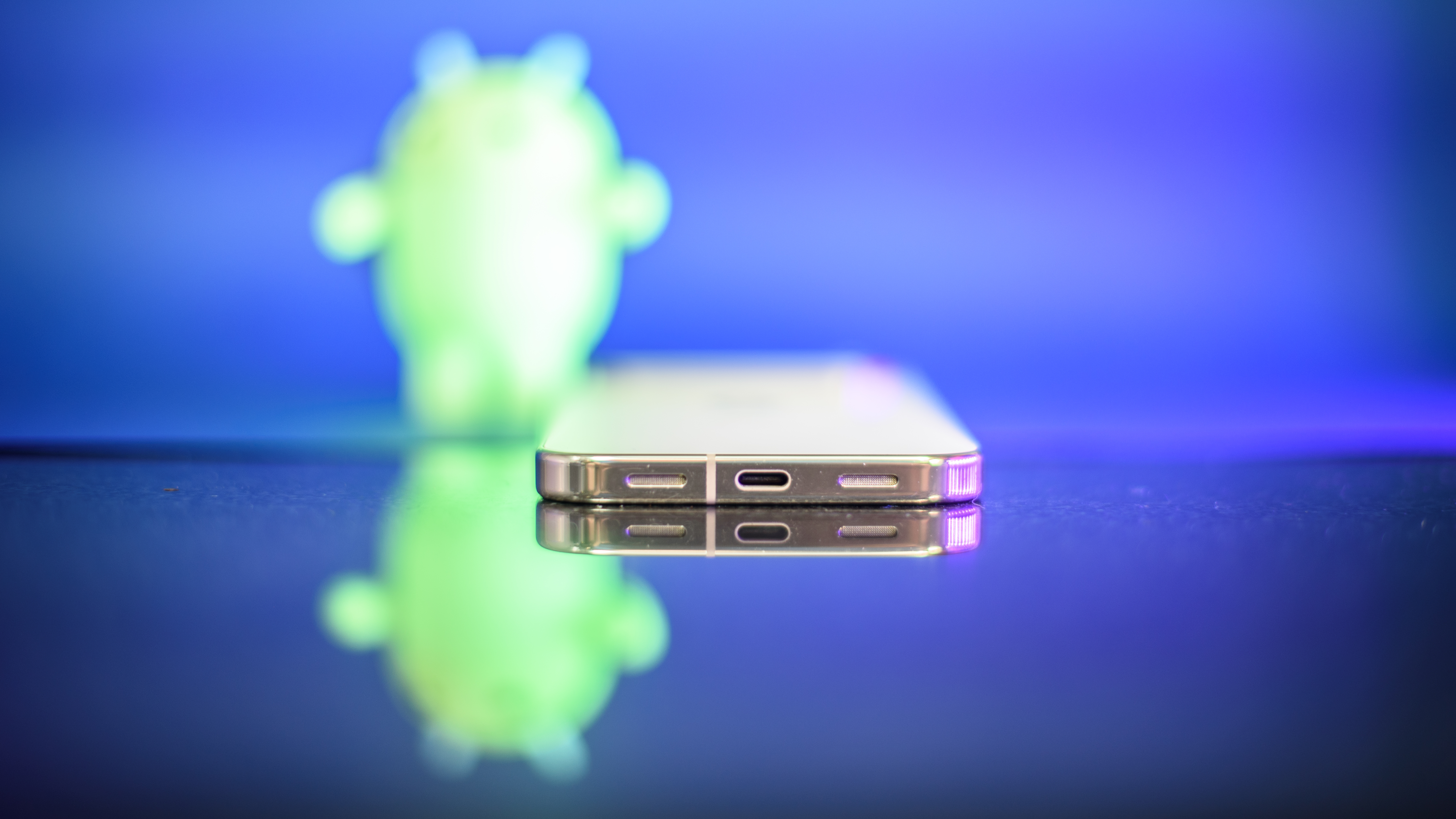 Google Pixel 10 Pro XL in Porcelain against a blue background with a green neon Android figurine in the background