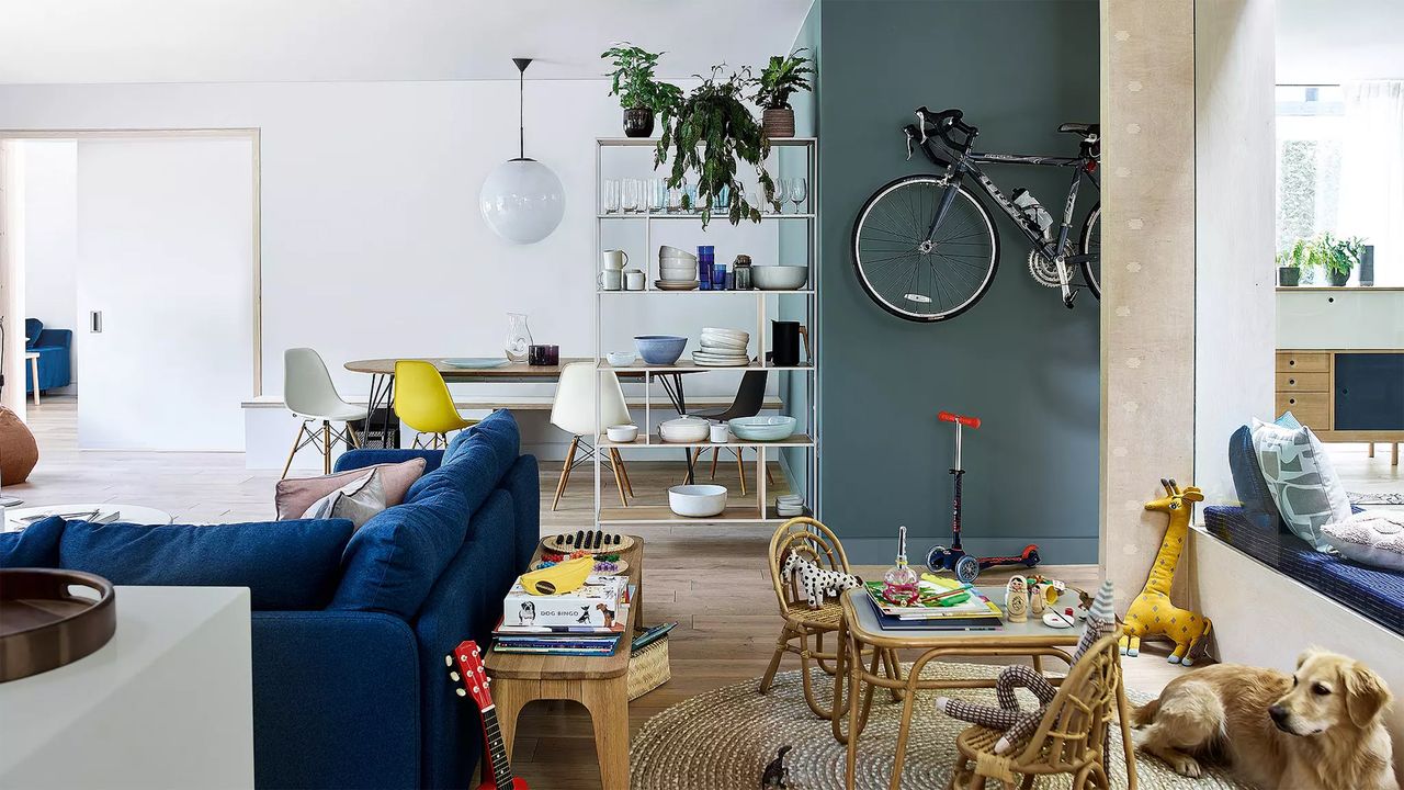 An open plan living room by John Lewis with blue velvet sofa, round dining room, modular shelves and play area