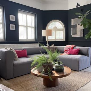 Black living room with large modular grey corner sofa and a walnut round coffee table