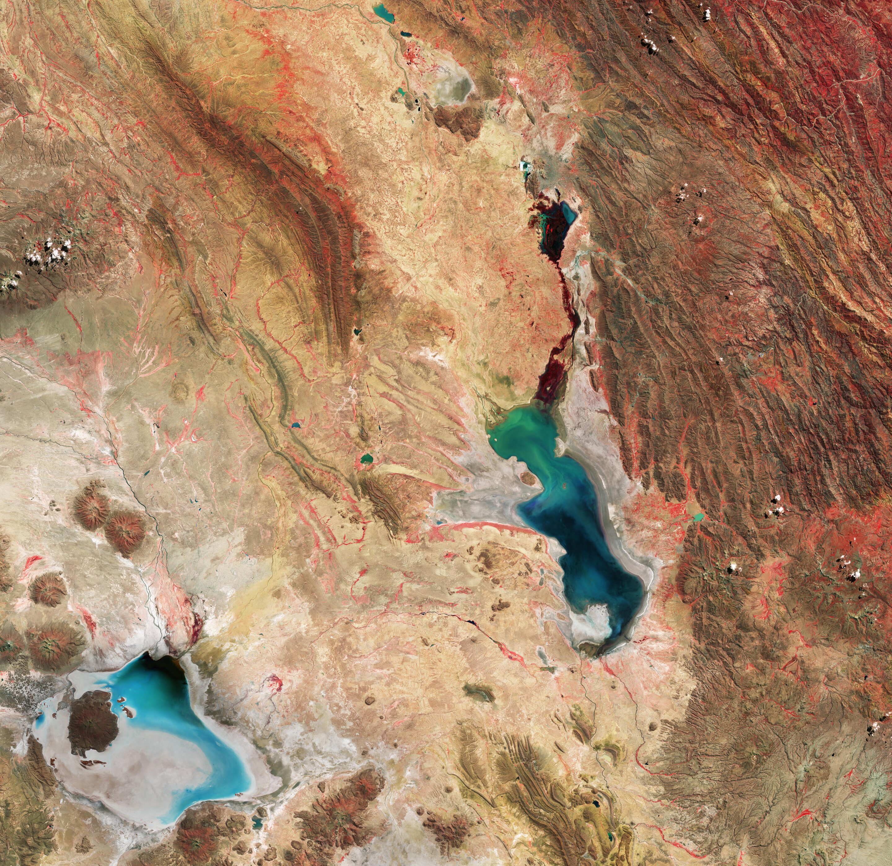 a aerial view of a brown and tan hilly and rocky terrain, with a pair of oddly shaped pools of vibrant blue and green water.