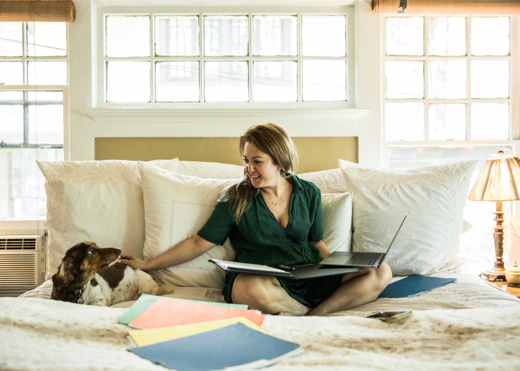 Woman working on laptop in bed with dog.