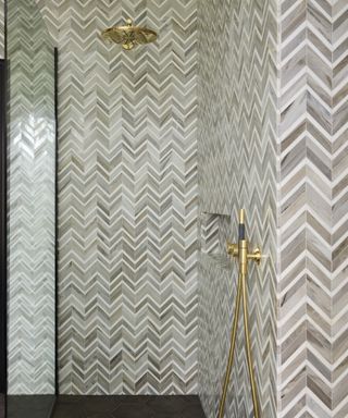 A walk-in shower with marble tiles arranged in a zig-zag pattern, and brass fittings – Shower tile ideas